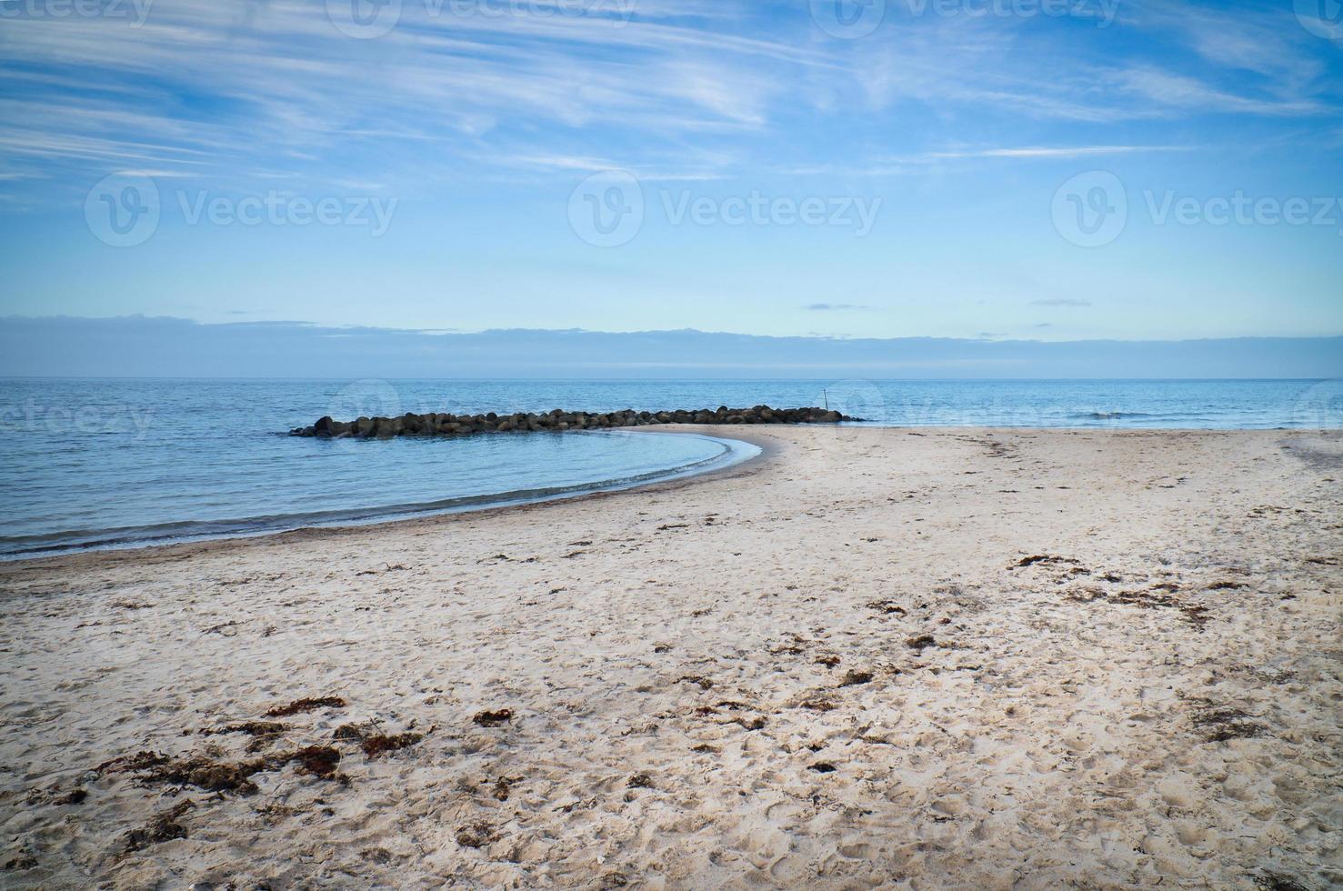 Sandy beach on the coast of Denmark. Stone groyne in the bay, sunshine while walking photo
