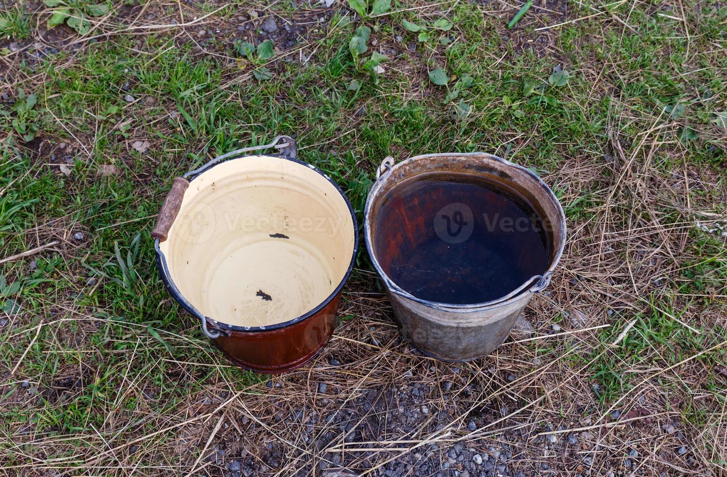 two iron buckets with clean water stand on the ground photo