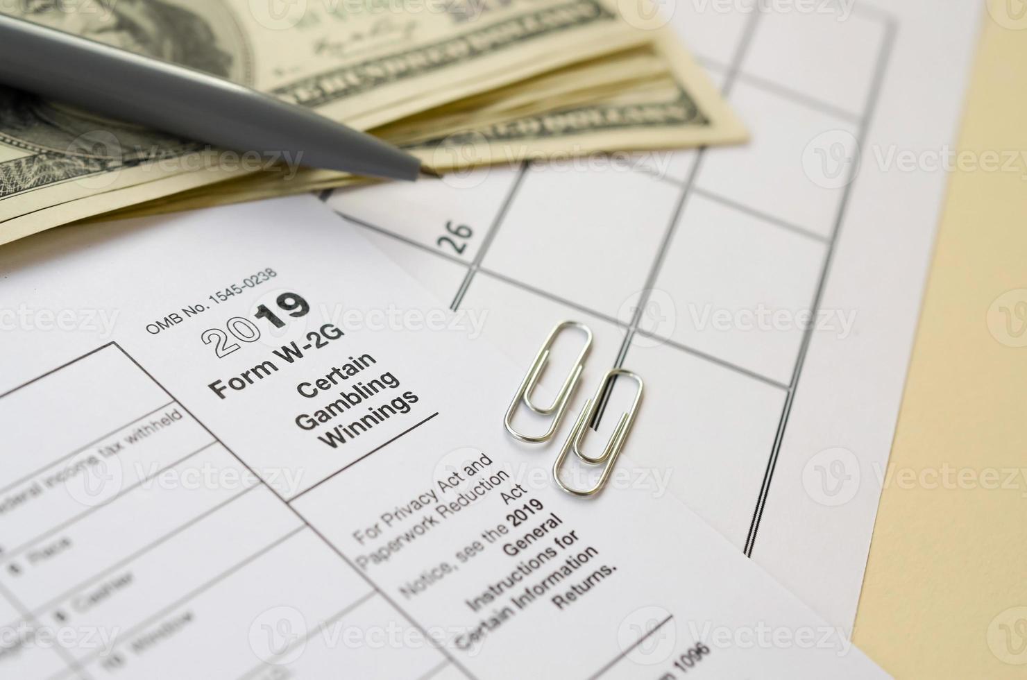 IRS Form W-2G Certain Gambling Winning blank lies with pen and many hundred dollar bills on calendar page photo