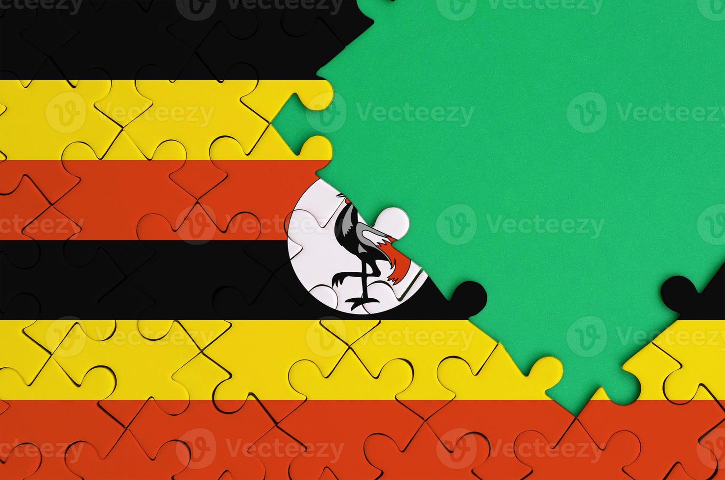 Uganda flag  is depicted on a completed jigsaw puzzle with free green copy space on the right side photo