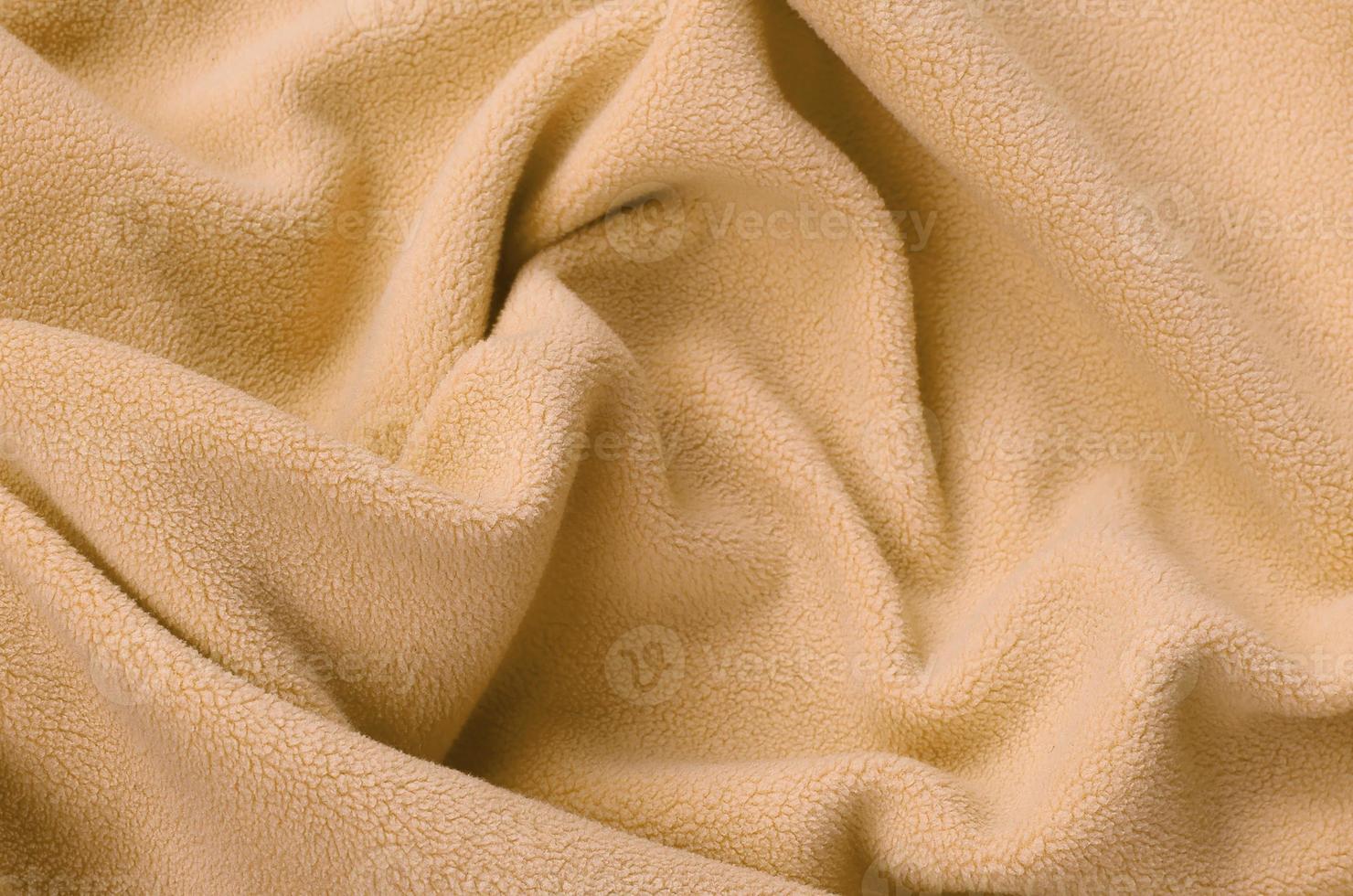 The blanket of furry orange fleece fabric. A background of light orange soft plush fleece material with a lot of relief folds photo