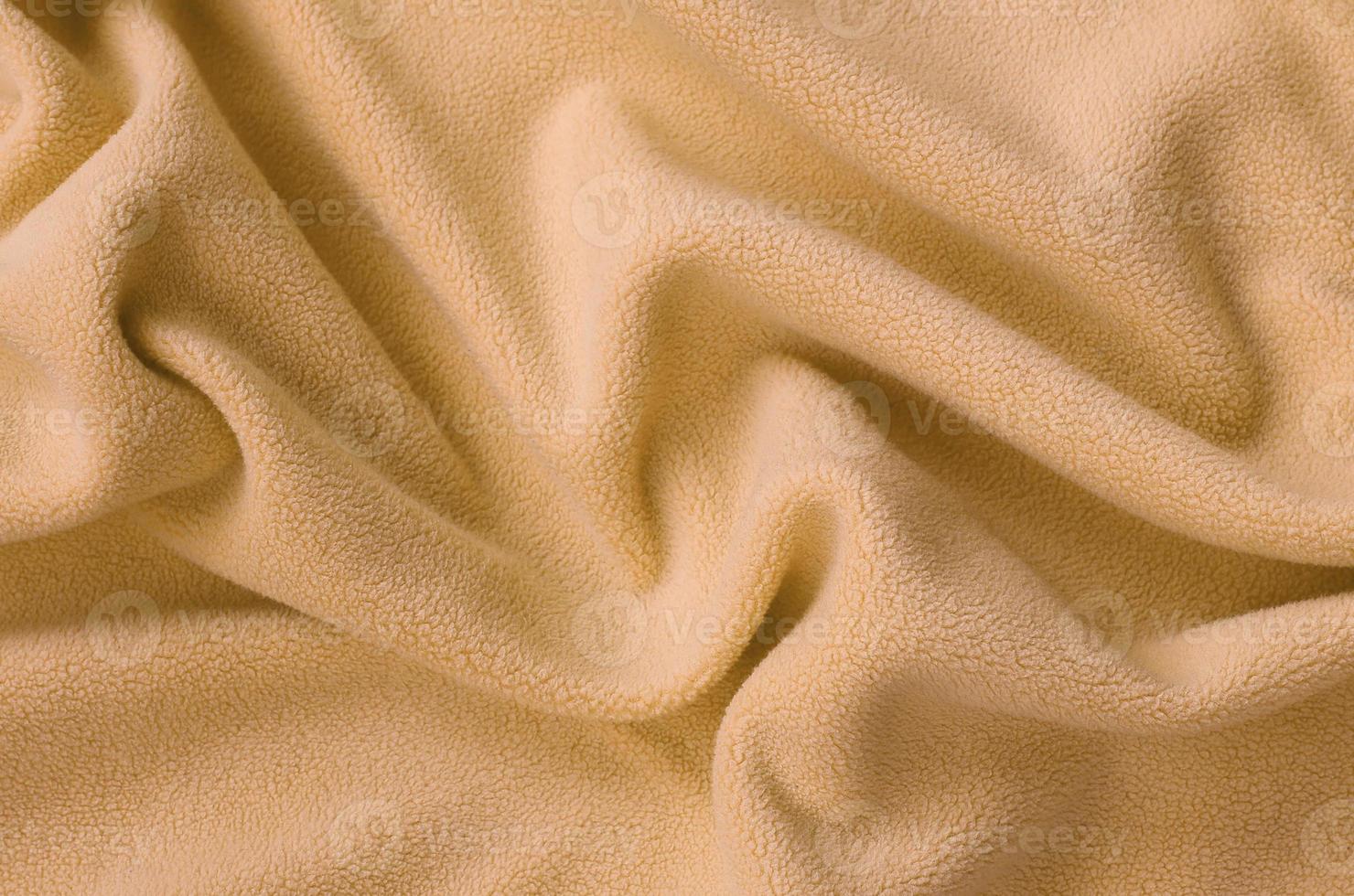 The blanket of furry orange fleece fabric. A background of light orange soft plush fleece material with a lot of relief folds photo