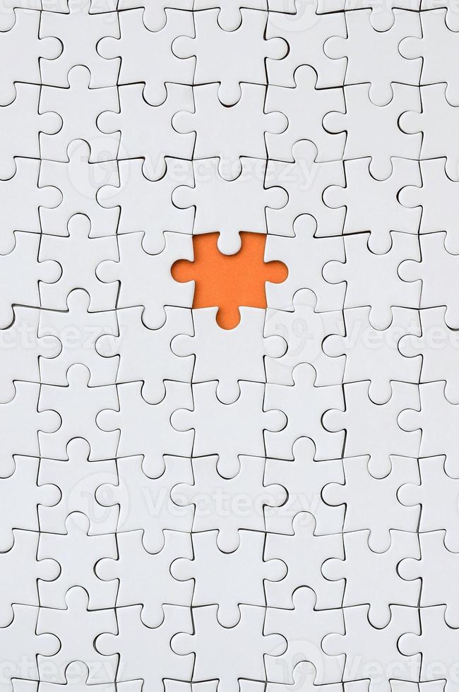 The texture of a white jigsaw puzzle in an assembled state with one missing element forming an orange space photo