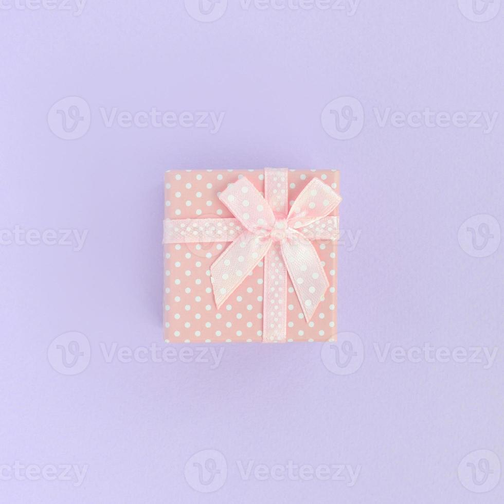 Small pink gift box with ribbon lies on a violet background. Minimalism flat lay top view photo