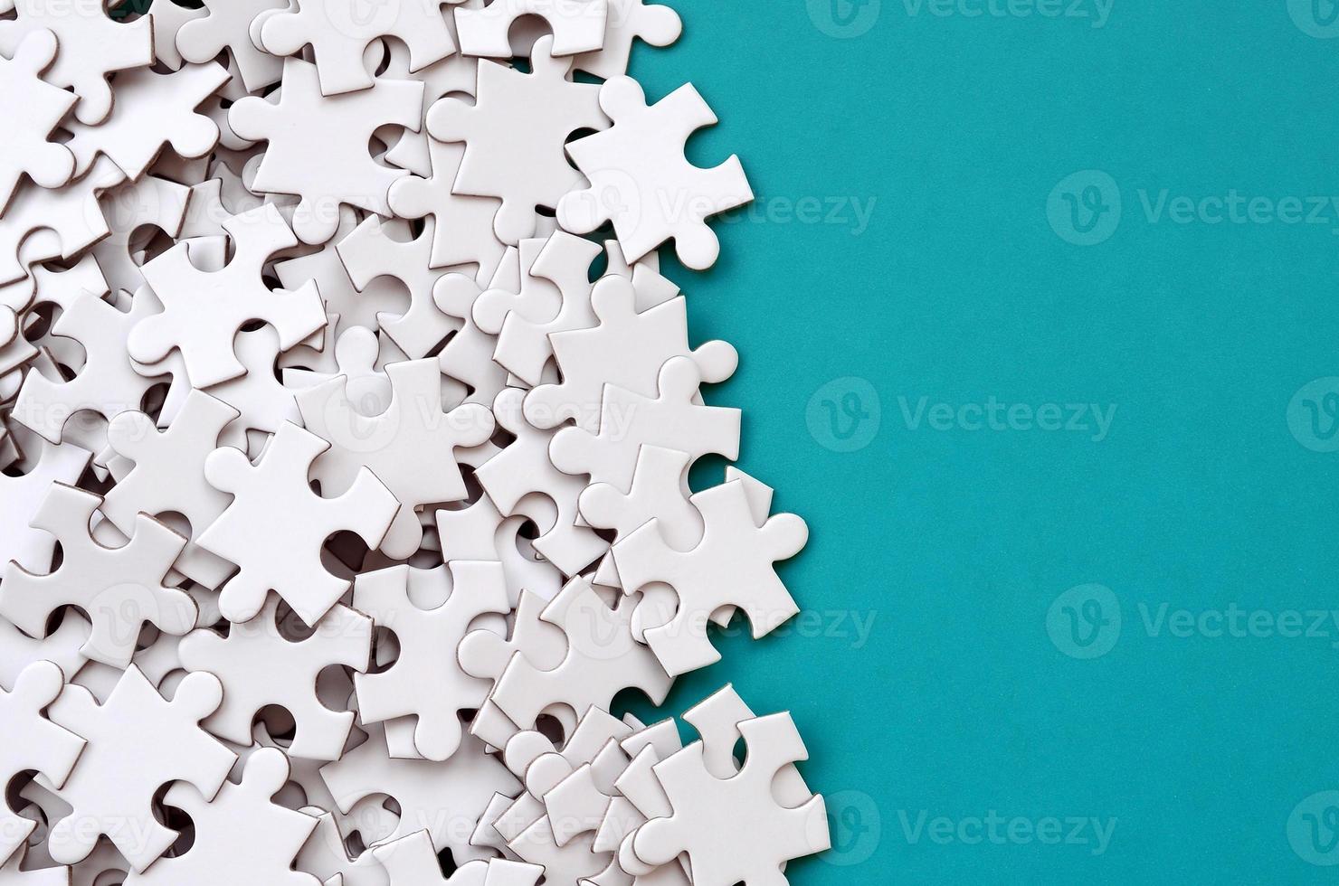 A pile of uncombed elements of a white jigsaw puzzle lies on the background of a blue surface. Texture photo with copy space for text