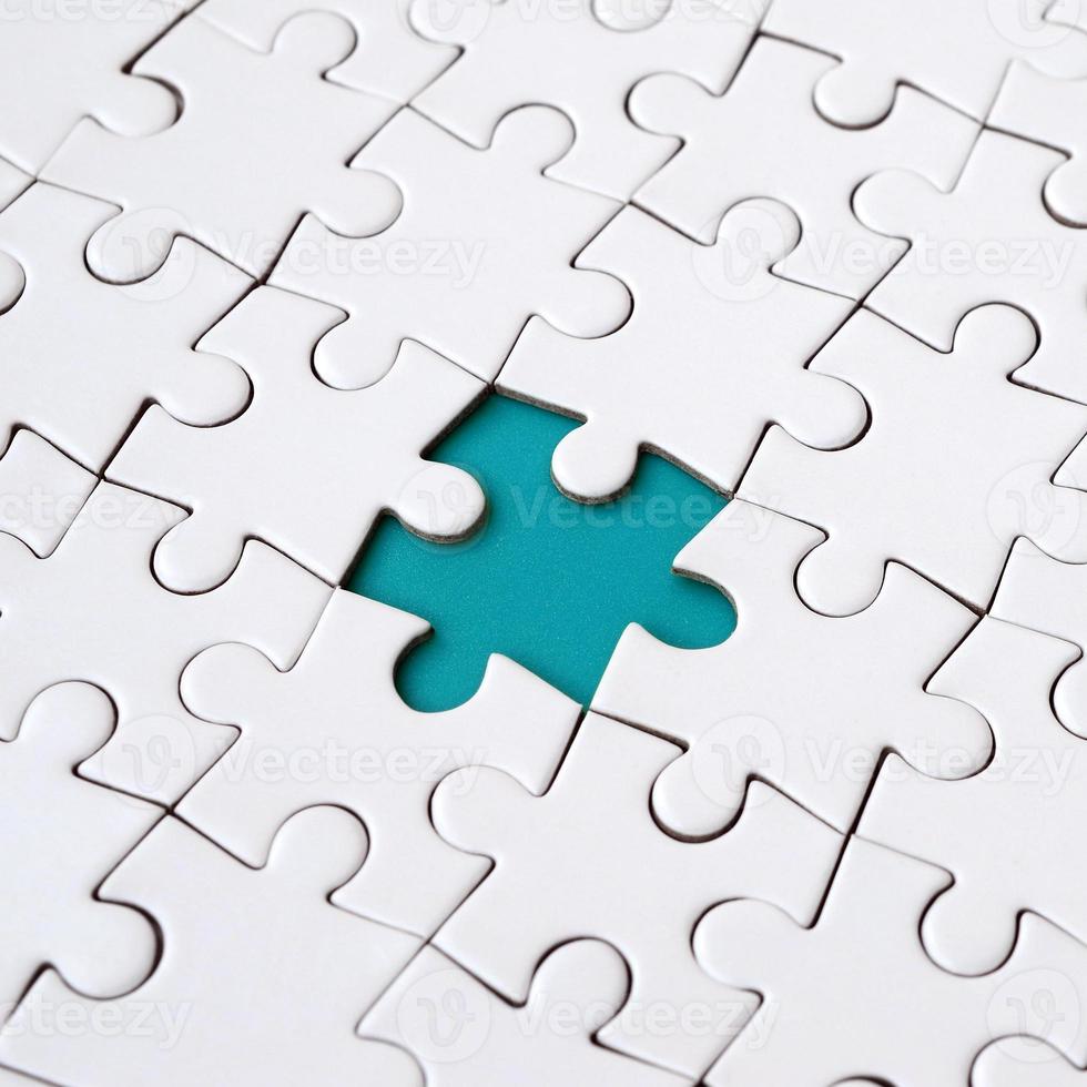 Close-up texture of a white jigsaw puzzle in assembled state with missing elements forming a blue pad for text. Copy space photo