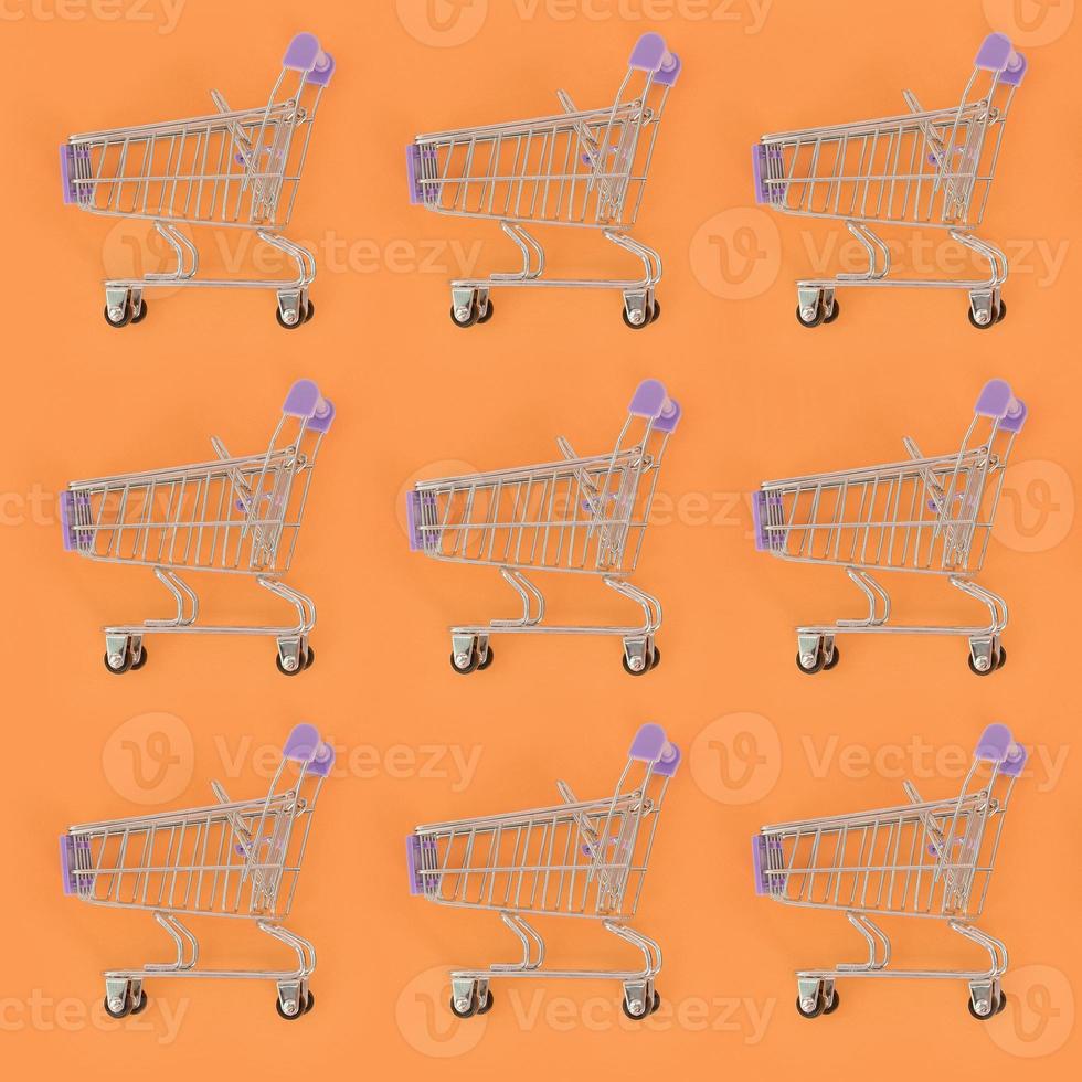 Shopping addiction, shopping lover or shopaholic concept. Many small empty shopping carts perform a pattern on a pastel colored paper background. Flat lay composition, top view photo