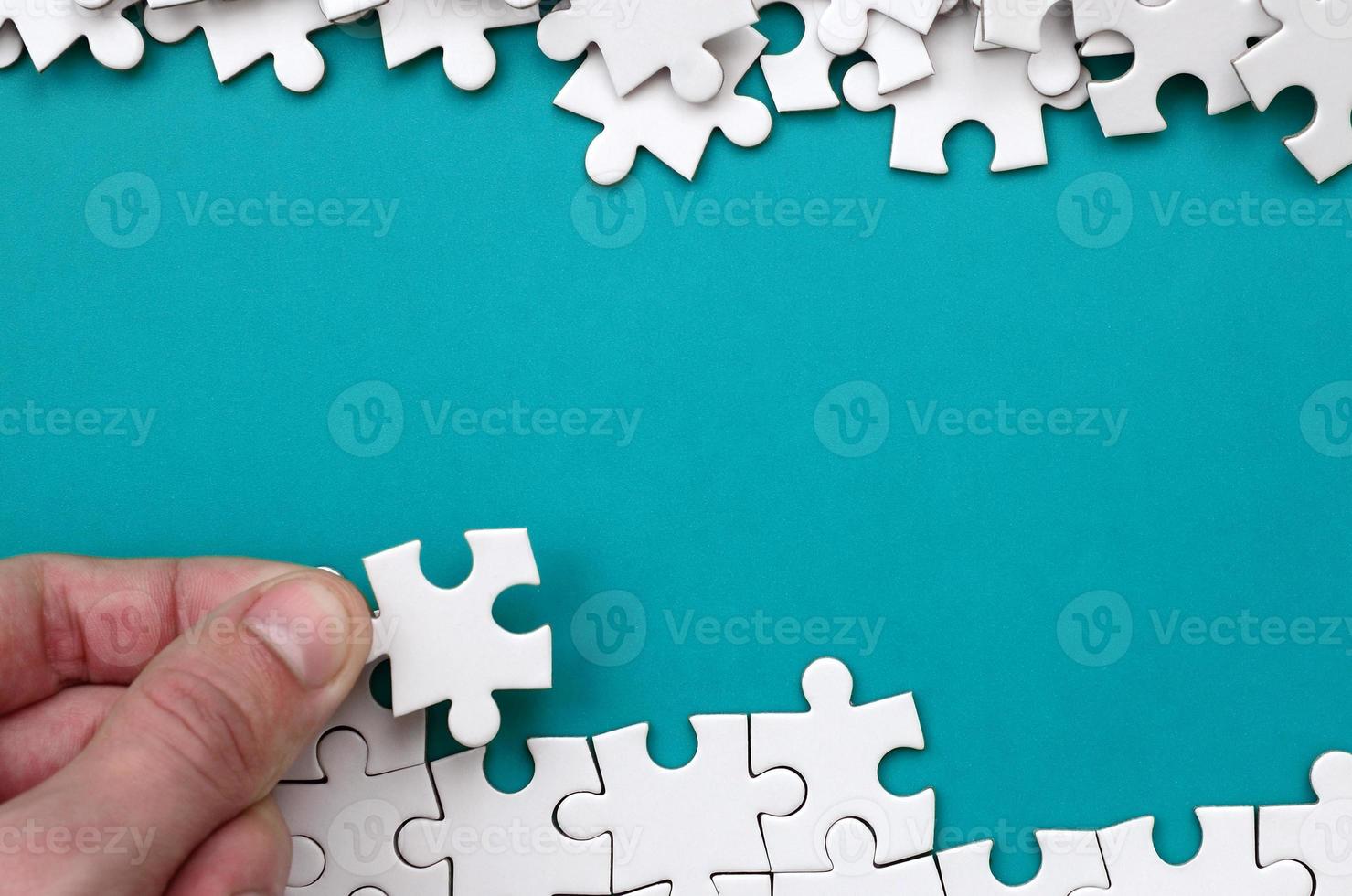 The hand folds a white jigsaw puzzle and a pile of uncombed puzzle pieces lies against the background of the blue surface. Texture photo with space for text