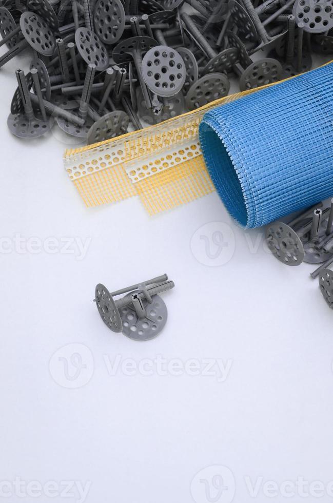 A set of construction items for the insulation of walls. Plastic dowels, a roll of mesh for the insulation of facades and a corner profile with a grid lie on the foam polystyrene surface photo