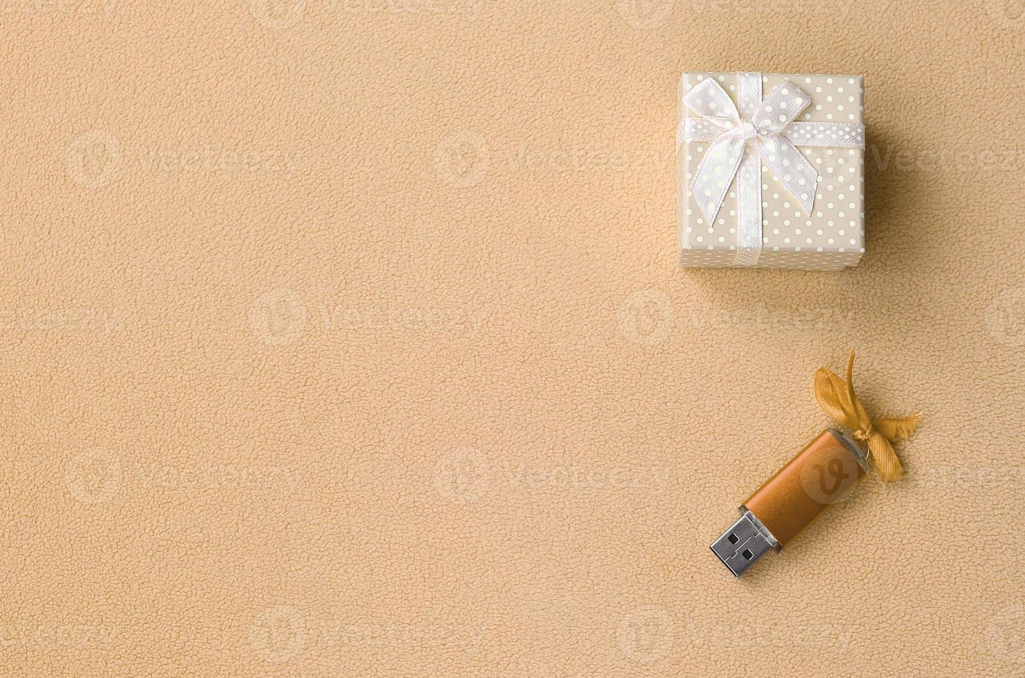 Orange usb memory card with a bow lies next to a small gift box in orange with a small bow on a blanket of soft and furry light fleece fabric. Classic fashion gift memory card design photo