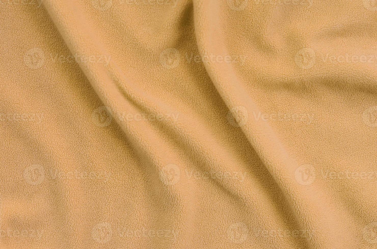 The blanket of furry orange fleece fabric. A background of light orange soft plush fleece material with a lot of relief folds photo