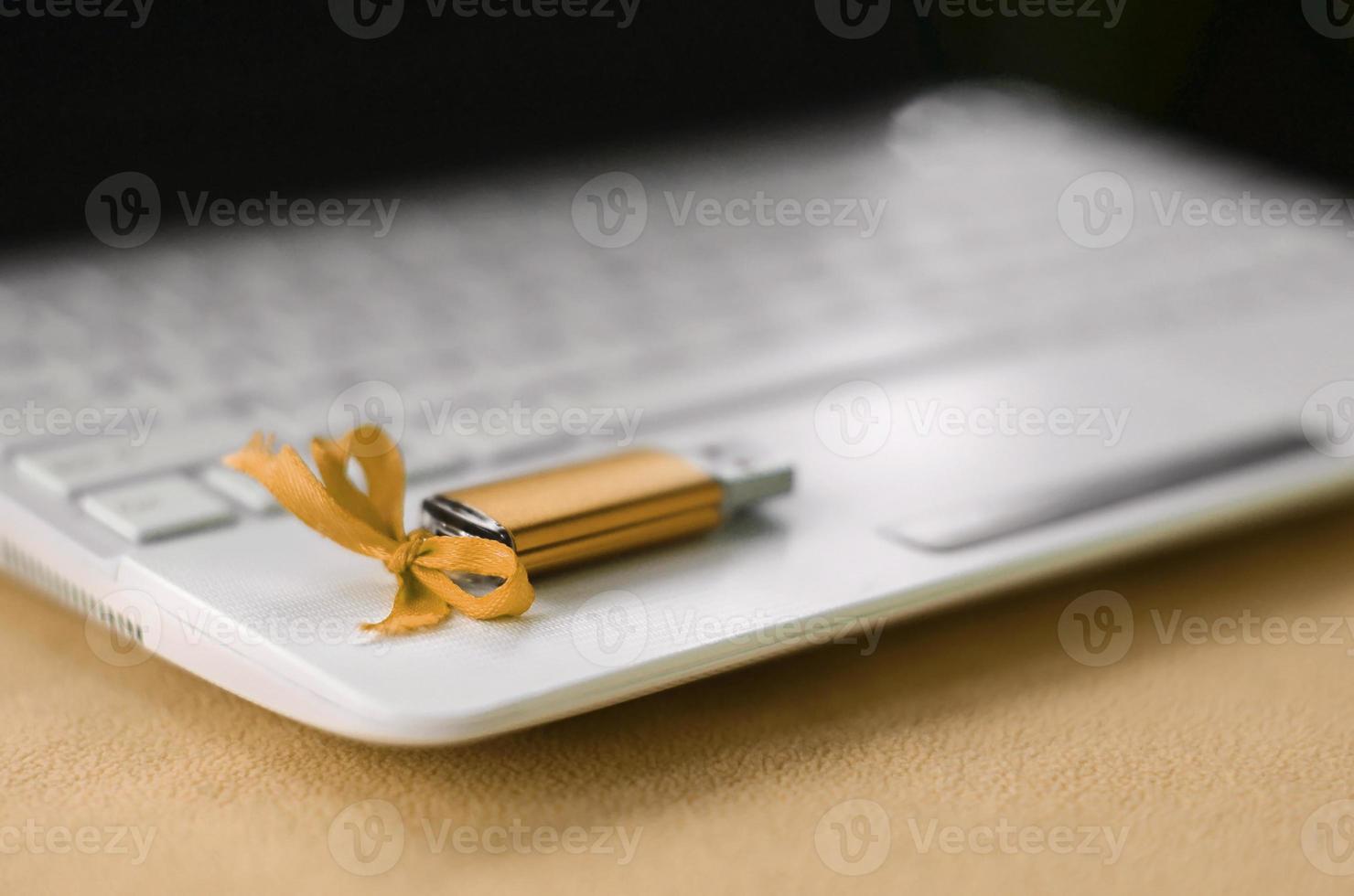 Orange usb flash memory card with a bow lies on a blanket of soft and furry light orange fleece fabric beside to a white laptop. Classic female gift design for a memory card photo