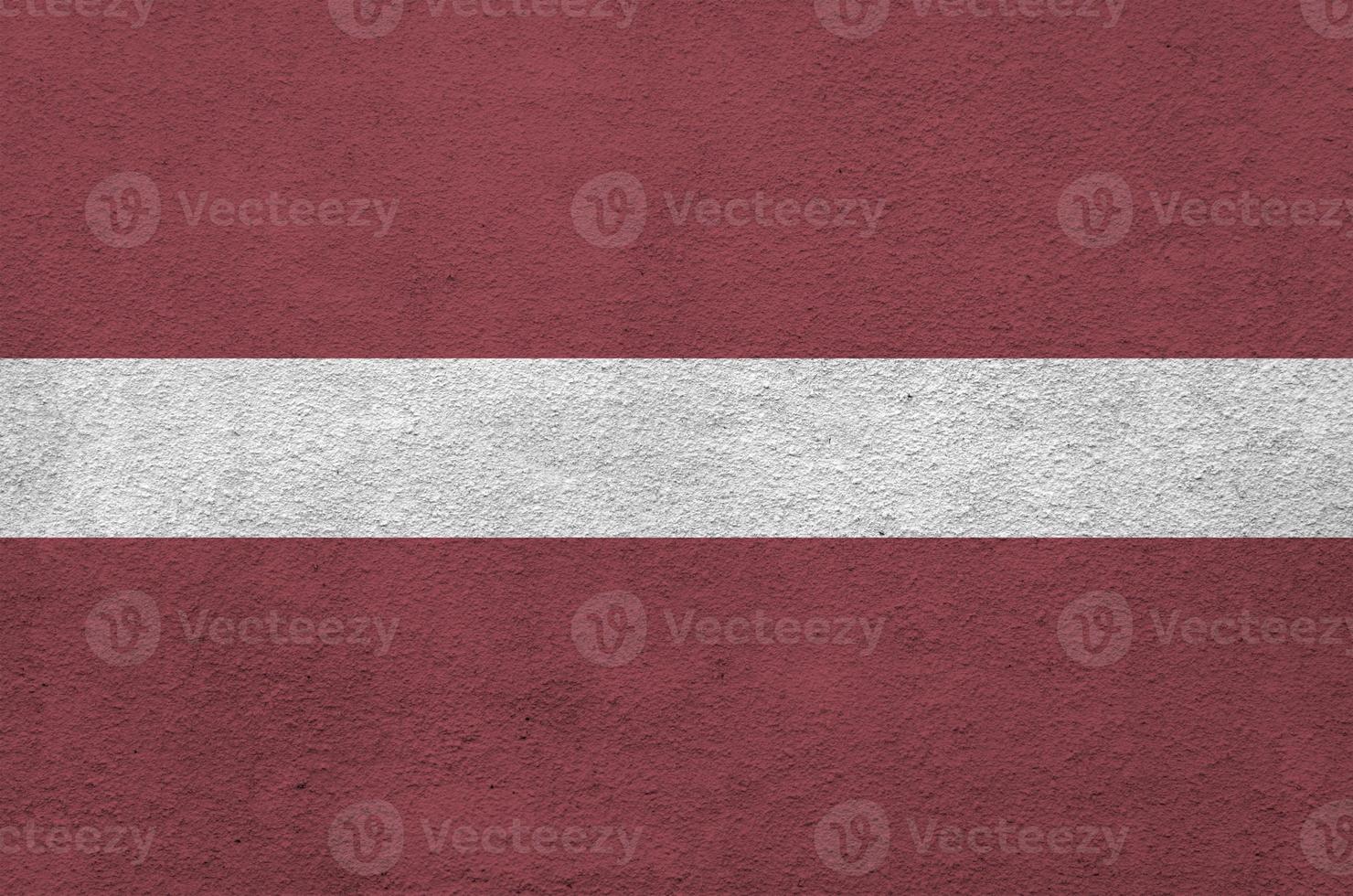 Latvia flag depicted in bright paint colors on old relief plastering wall. Textured banner on rough background photo