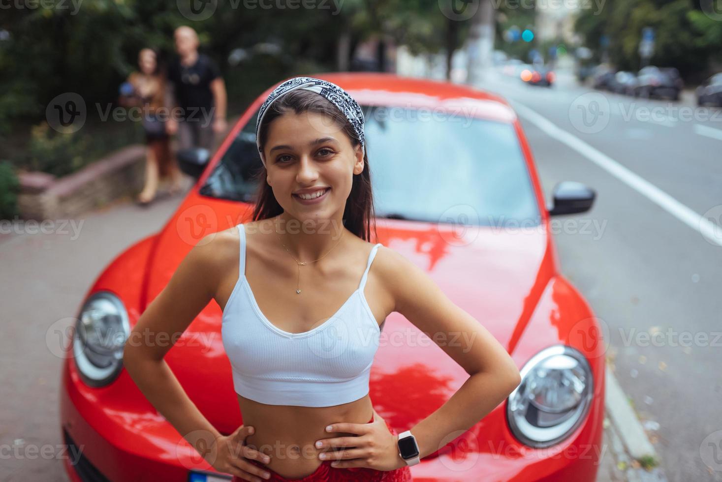 retrato de una mujer bastante caucásica parada contra un auto rojo nuevo foto