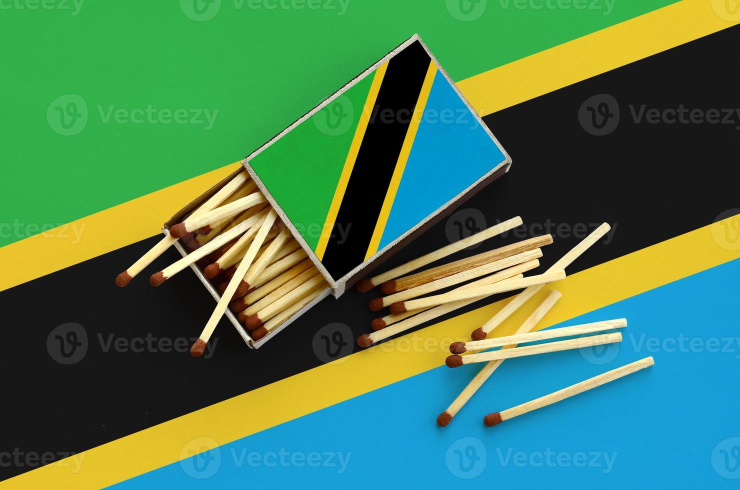 Tanzania flag  is shown on an open matchbox, from which several matches fall and lies on a large flag photo