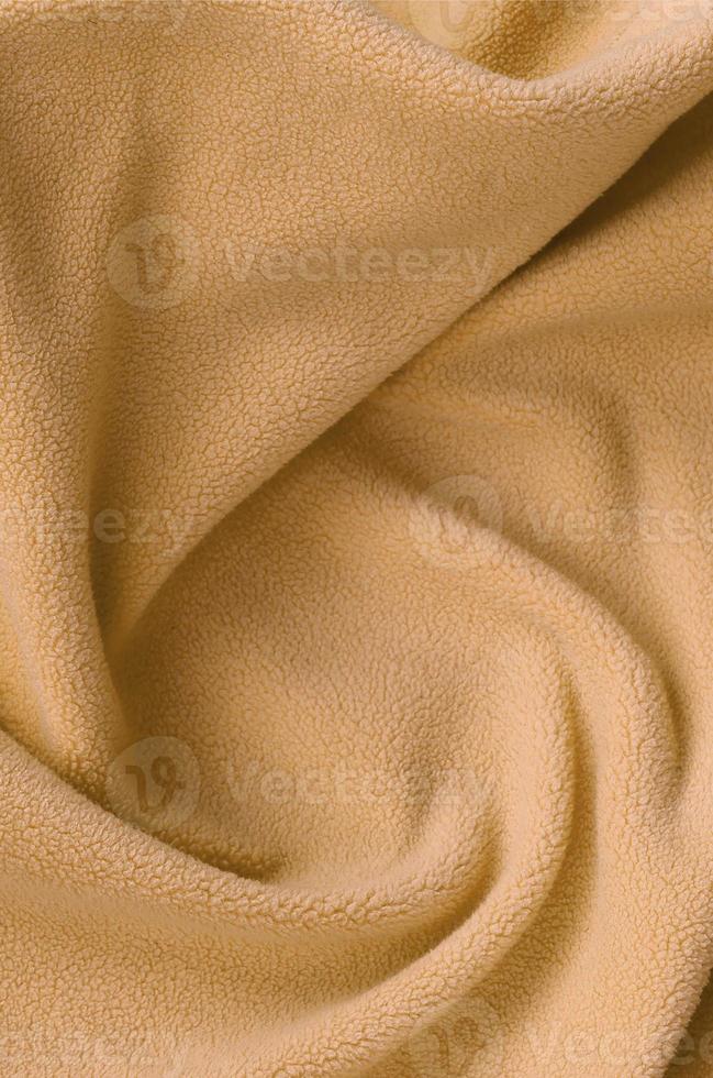 The blanket of furry orange fleece fabric. A background of light orange soft plush fleece material with a lot of relief folds photo
