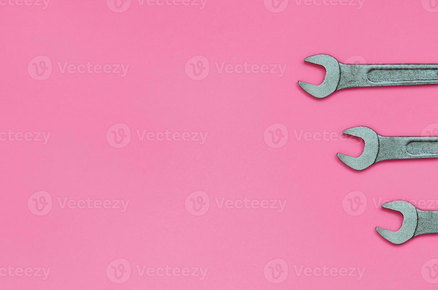 Three metallic spanners lie on texture background of fashion pastel pink color paper in minimal concept photo