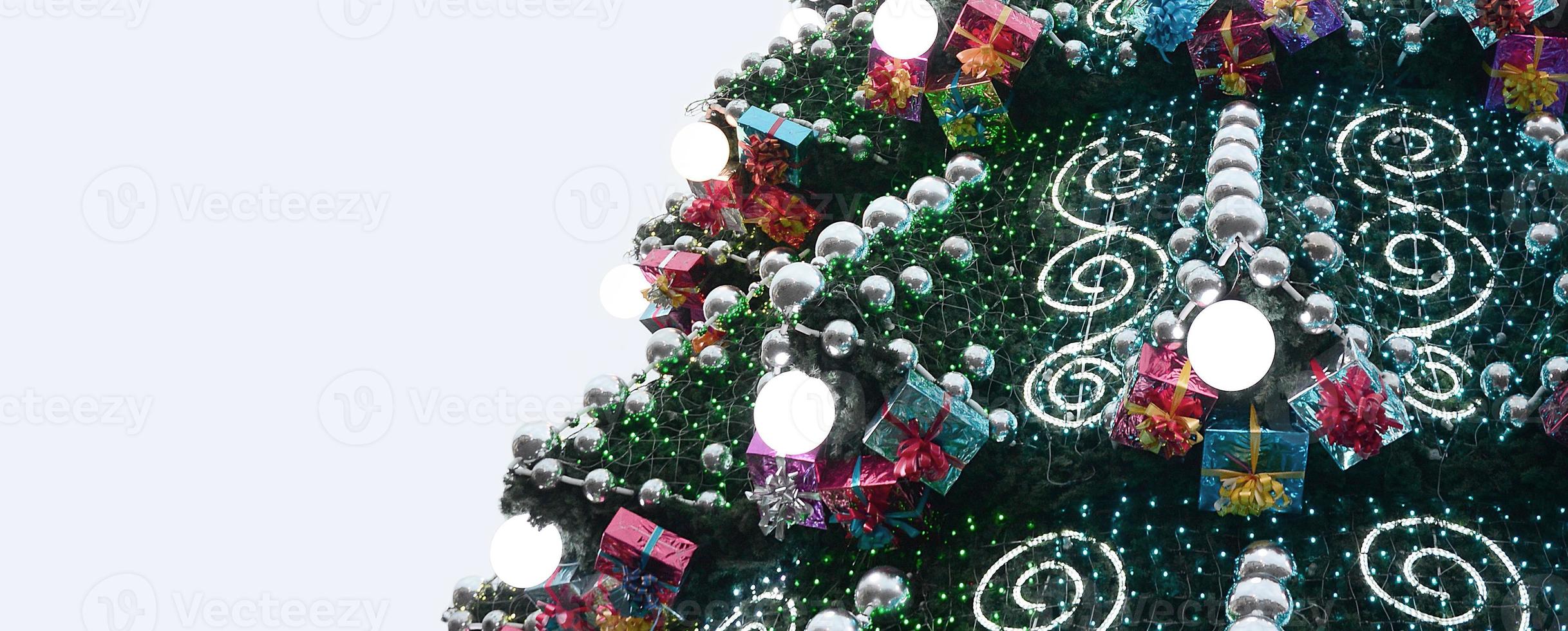 A fragment of a huge Christmas tree with many ornaments, gift boxes and luminous lamps. Photo of a decorated Christmas tree close-up with copy space