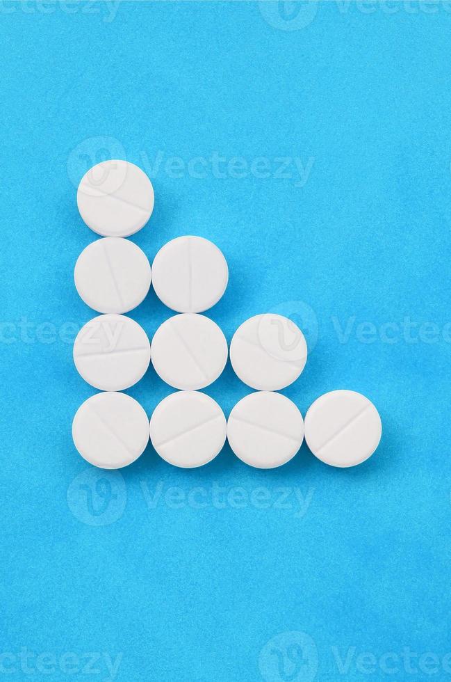 Several white tablets lie on a bright blue background in the form of a triangular arrow. Background image on medicine and pharmaceutical topics photo