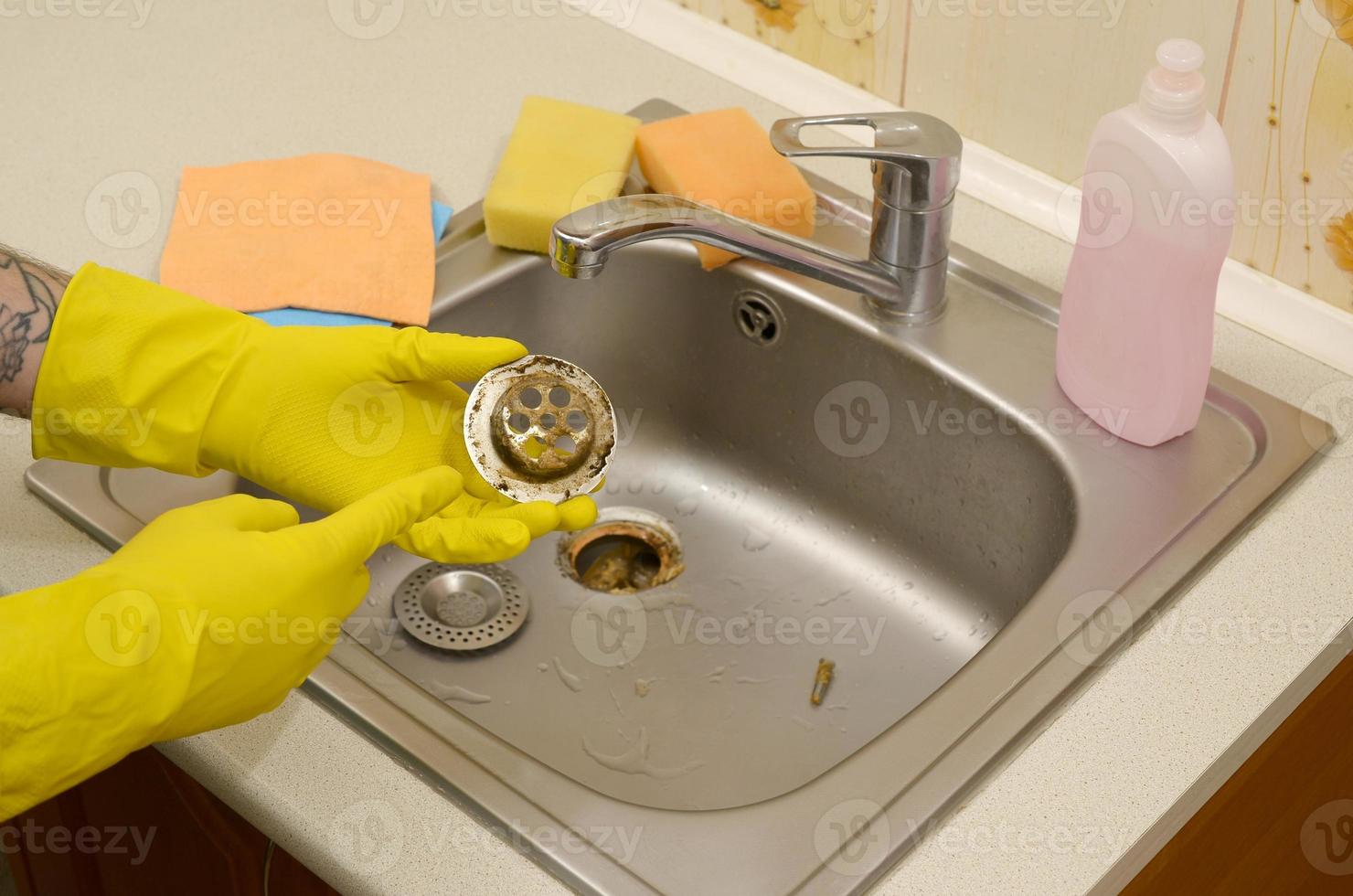 limpiador en guantes de goma muestra residuos en el protector de desagües de un fregadero de cocina foto