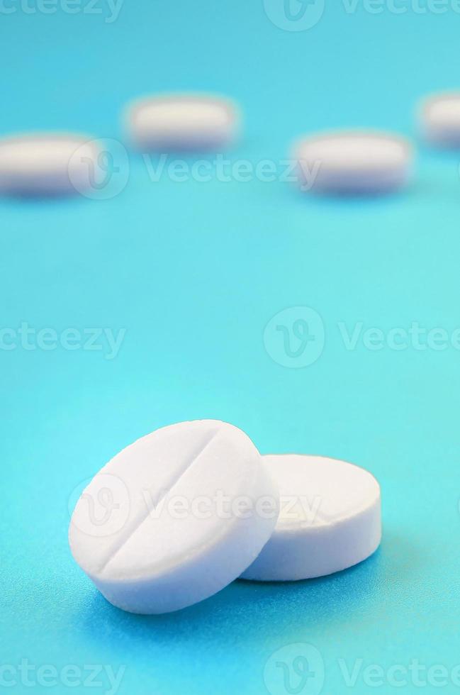 A few white tablets lie on a bright blue background surface. Background image on medical and pharmaceutical topics photo