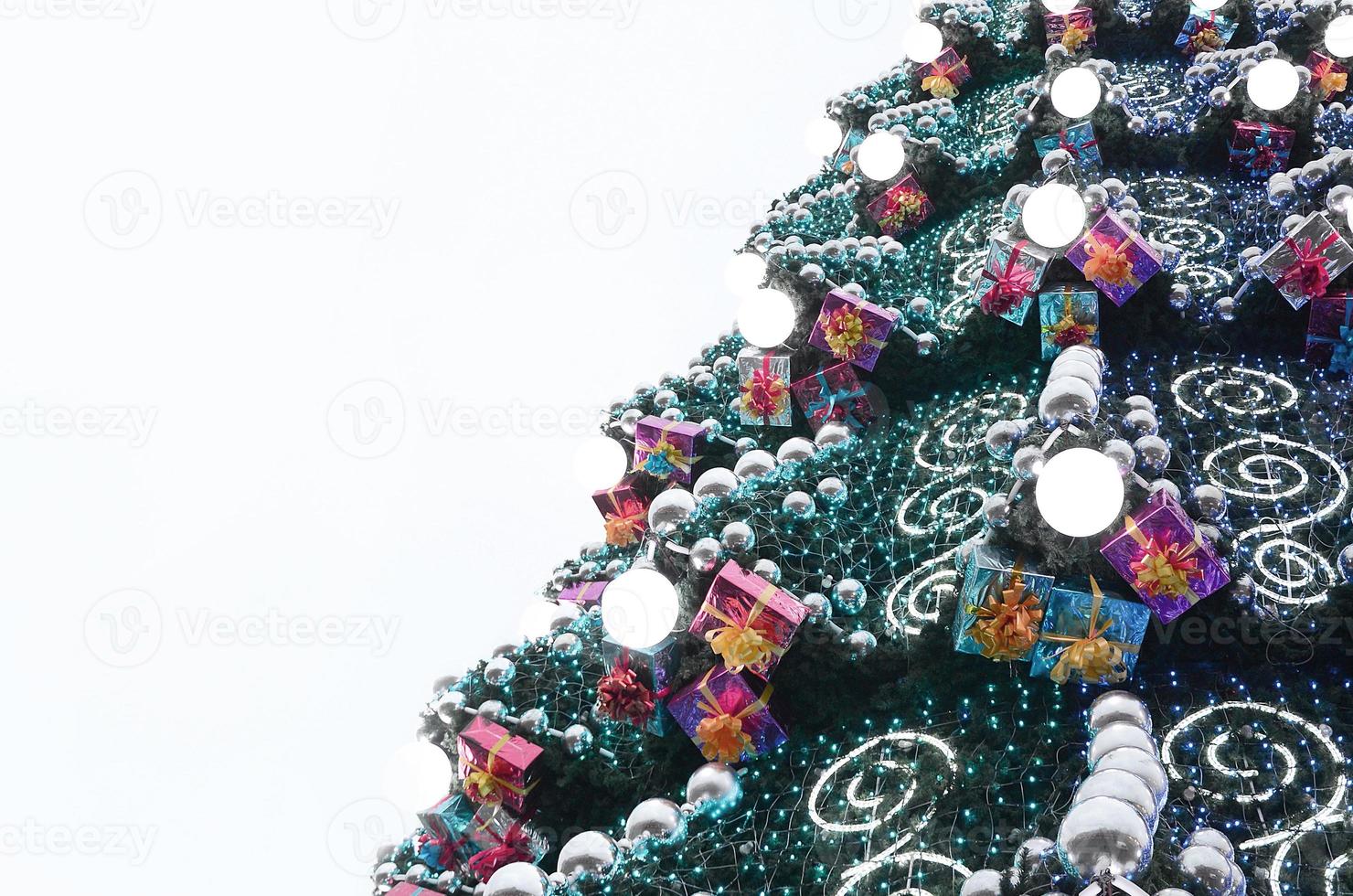 A fragment of a huge Christmas tree with many ornaments, gift boxes and luminous lamps. Photo of a decorated Christmas tree close-up with copy space