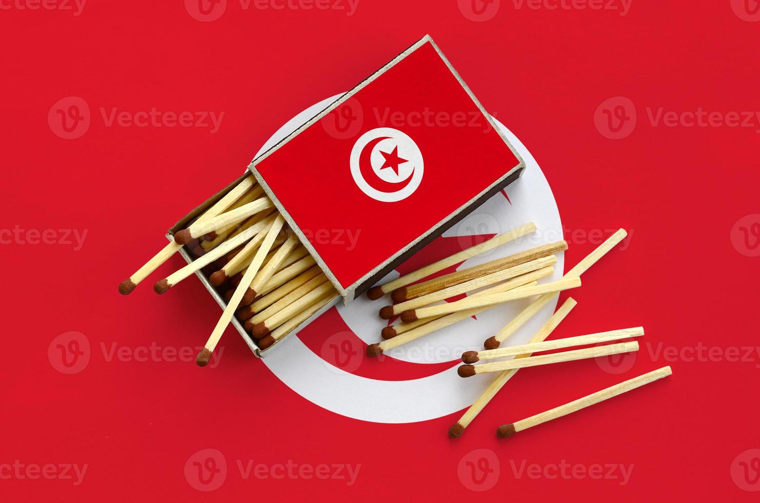 Tunisia flag  is shown on an open matchbox, from which several matches fall and lies on a large flag photo
