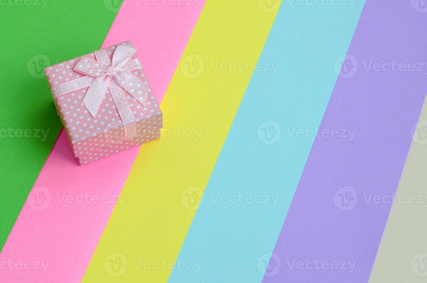 Small pink gift box lie on texture background of fashion pastel pink, blue, green, yellow, violet and beige colors paper in minimal concept. Abstract trendy pattern photo