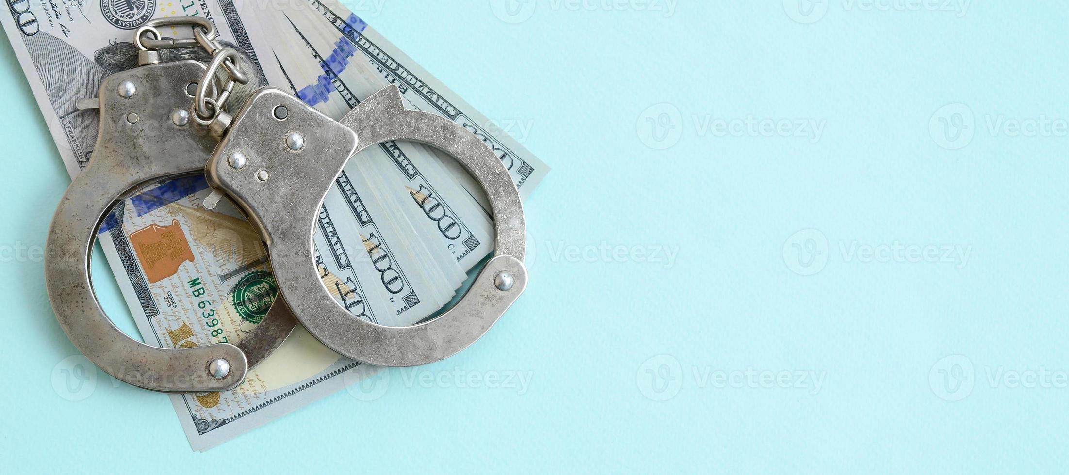 Silver police handcuffs and hundred dollar bills lies on light blue background photo