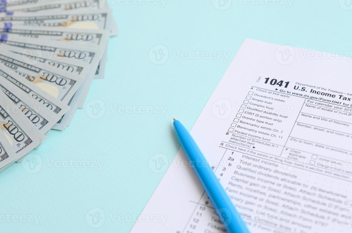 1041 tax form lies near hundred dollar bills and blue pen on a light blue background. US Income tax return for estates and trusts photo