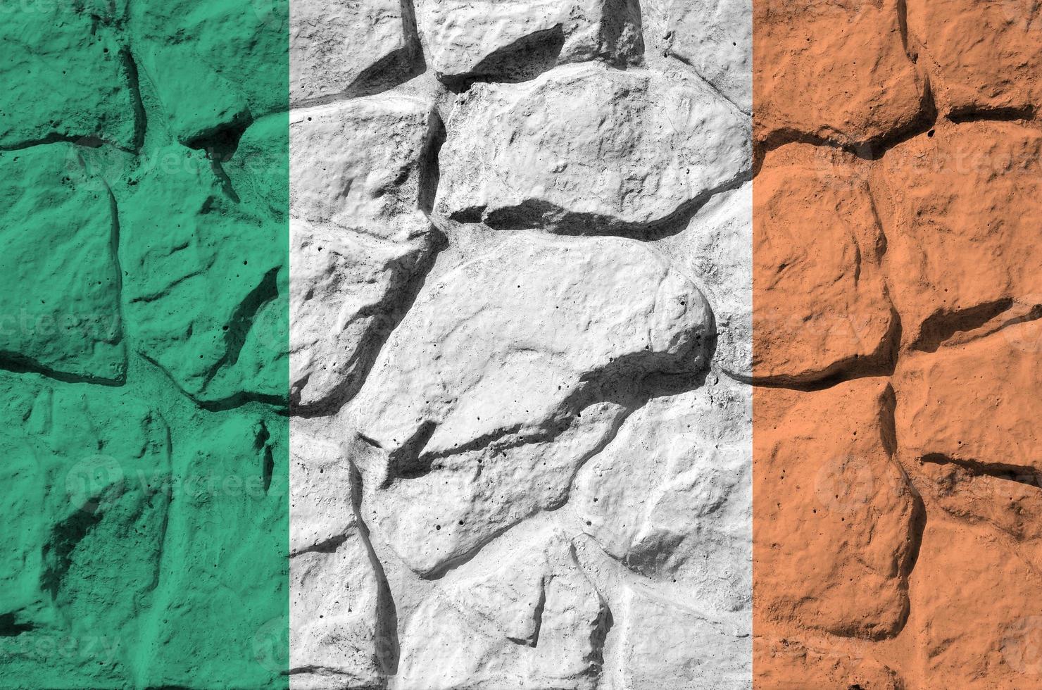 bandera de irlanda representada en colores de pintura en el primer plano de la pared de piedra antigua. banner texturizado sobre fondo de pared de roca foto