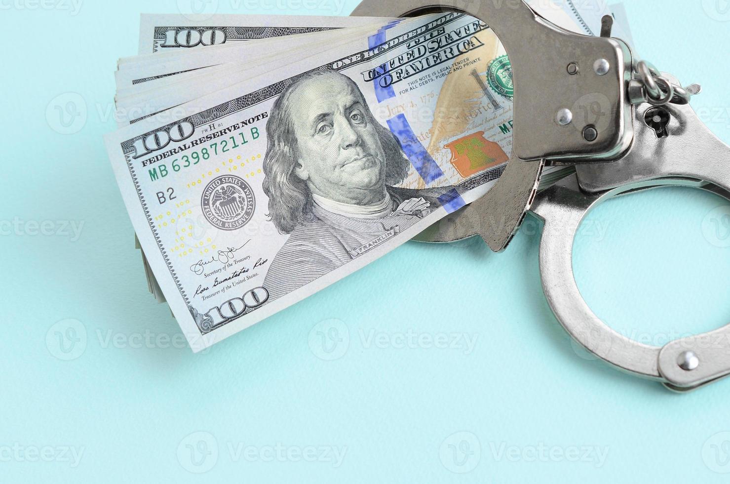 Silver police handcuffs and hundred dollar bills lies on light blue background photo