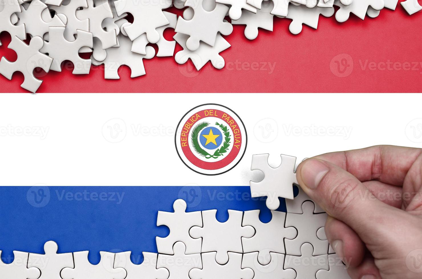 la bandera de paraguay está representada en una mesa en la que la mano humana dobla un rompecabezas de color blanco foto