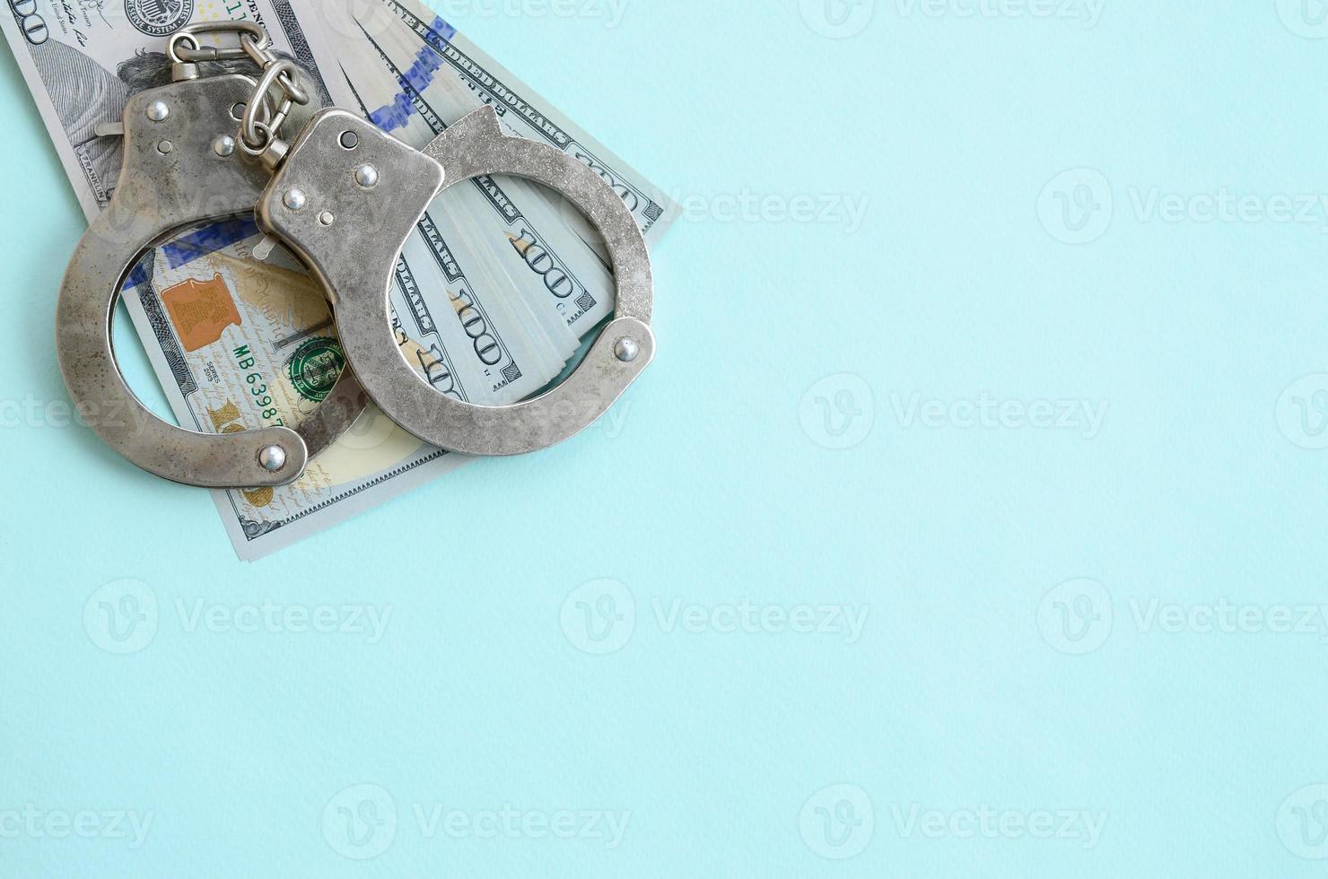 Silver police handcuffs and hundred dollar bills lies on light blue background photo