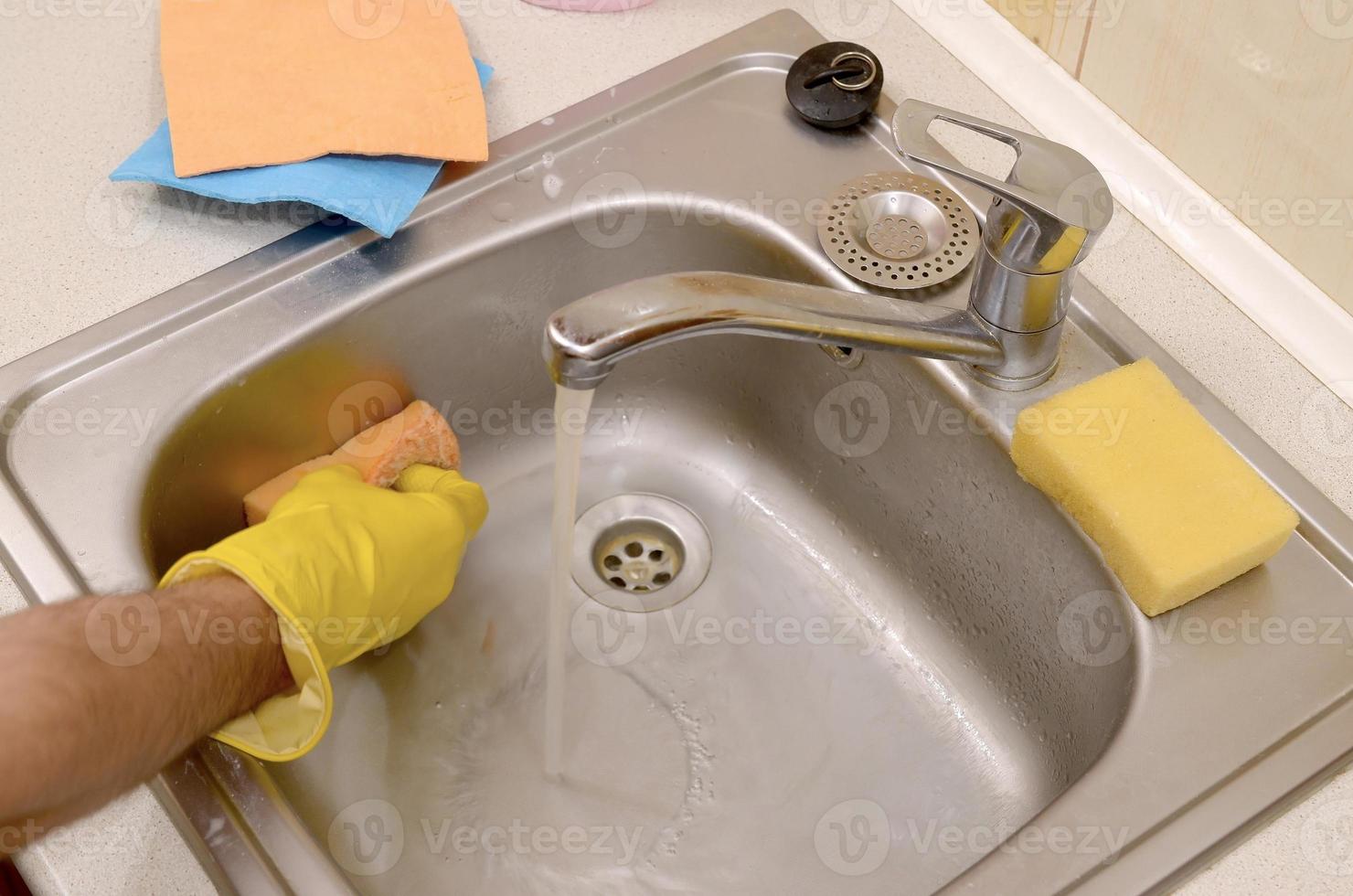 Person or householder cleaning the kitchen sink with sponge in close up view photo