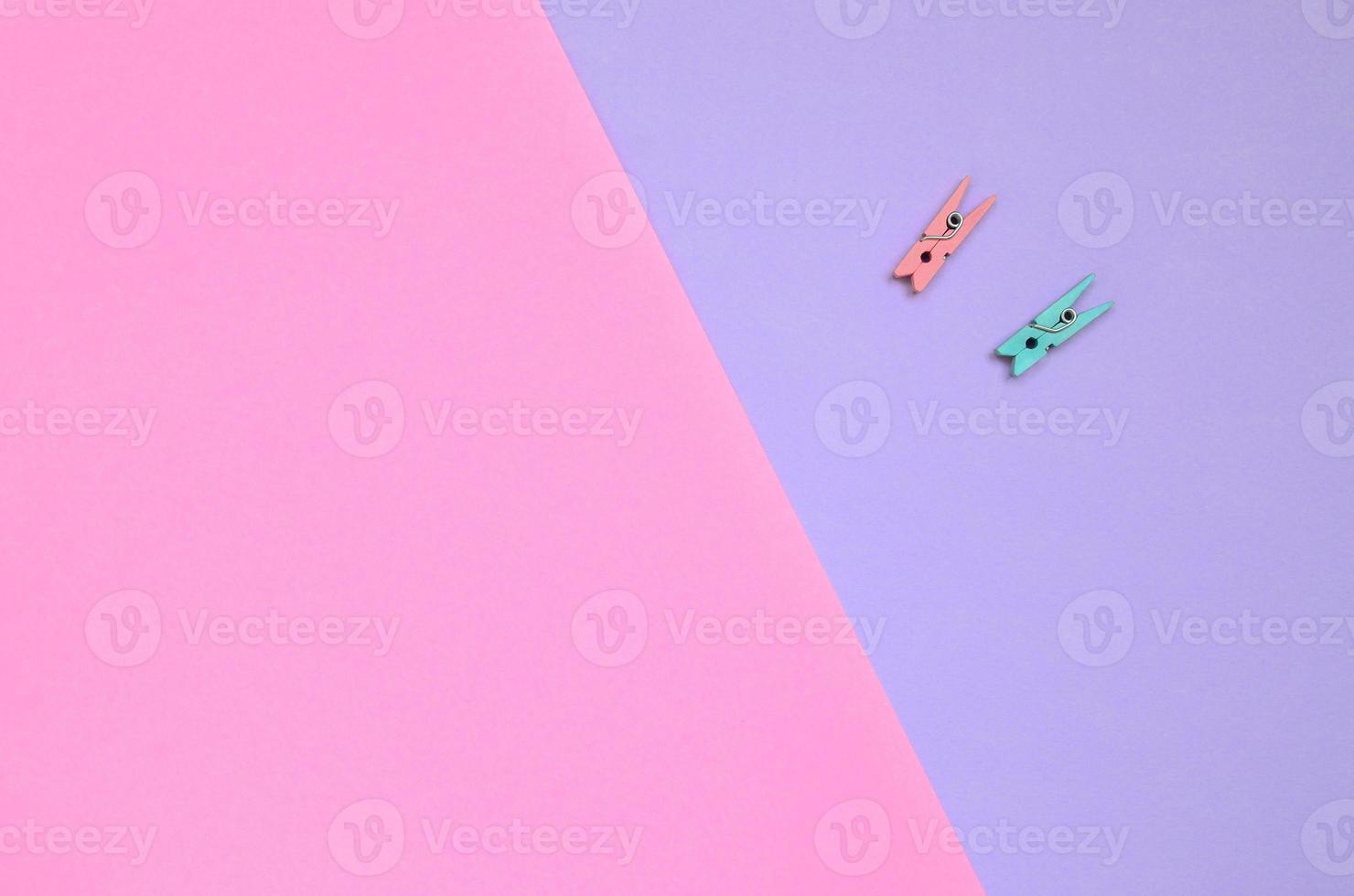 Two colored wooden pegs lie on texture background of fashion pastel violet and pink colors paper in minimal concept photo