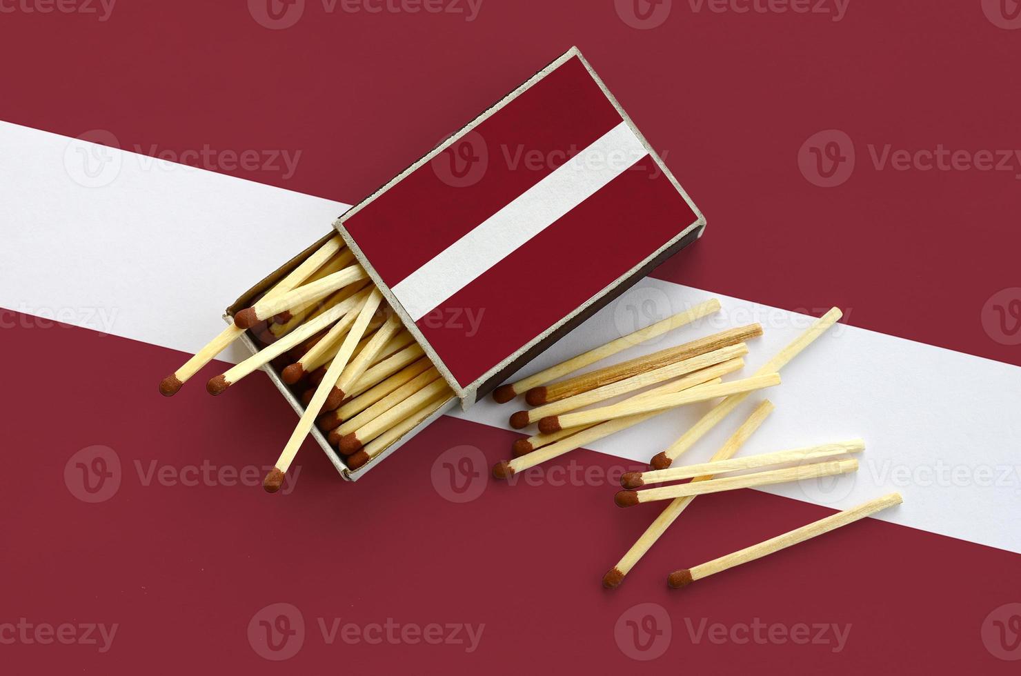 Latvia flag  is shown on an open matchbox, from which several matches fall and lies on a large flag photo