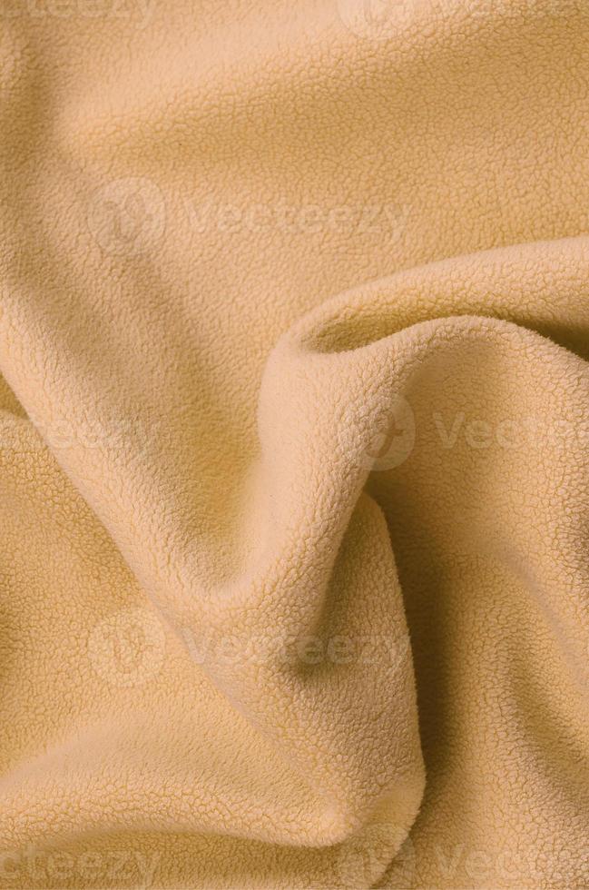 The blanket of furry orange fleece fabric. A background of light orange soft plush fleece material with a lot of relief folds photo