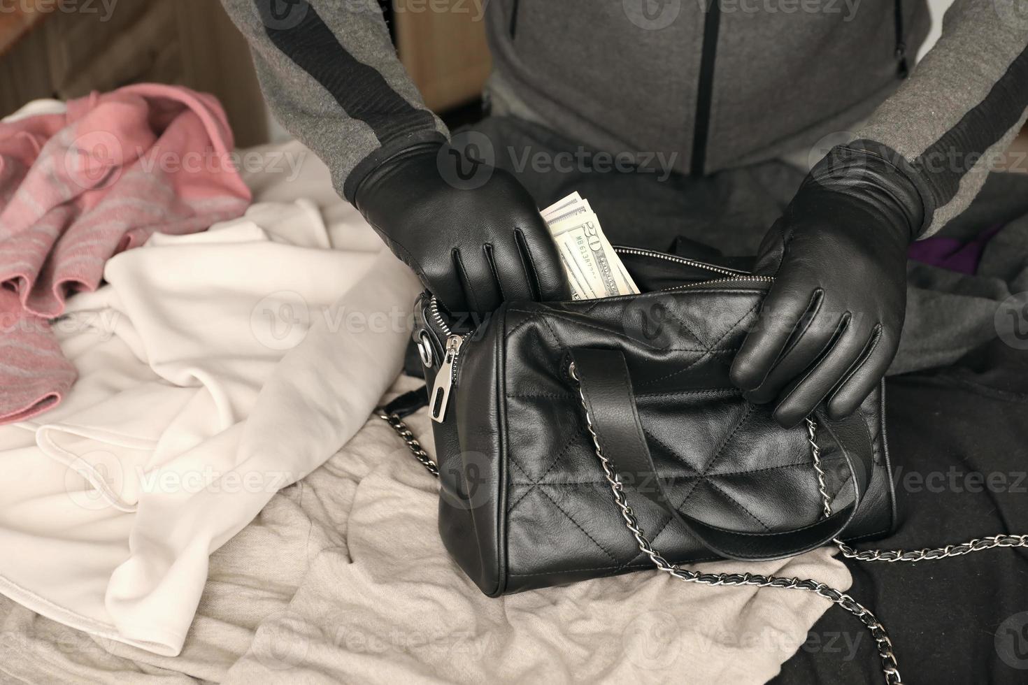 Robber in black outfit and gloves see in opened stolen women bag. The thief takes out US dollar bills from a womans handbag in kitchen photo