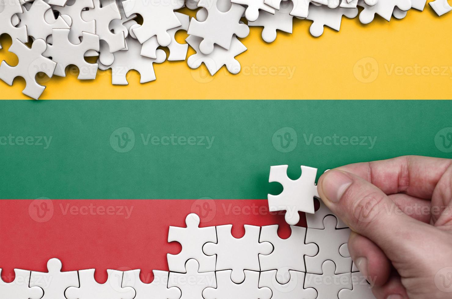Lithuania flag  is depicted on a table on which the human hand folds a puzzle of white color photo