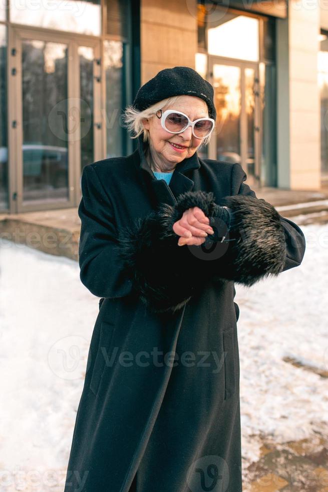 senior stylish woman in beret and elegant black coat going to the business appointment. Business, style, age concept photo