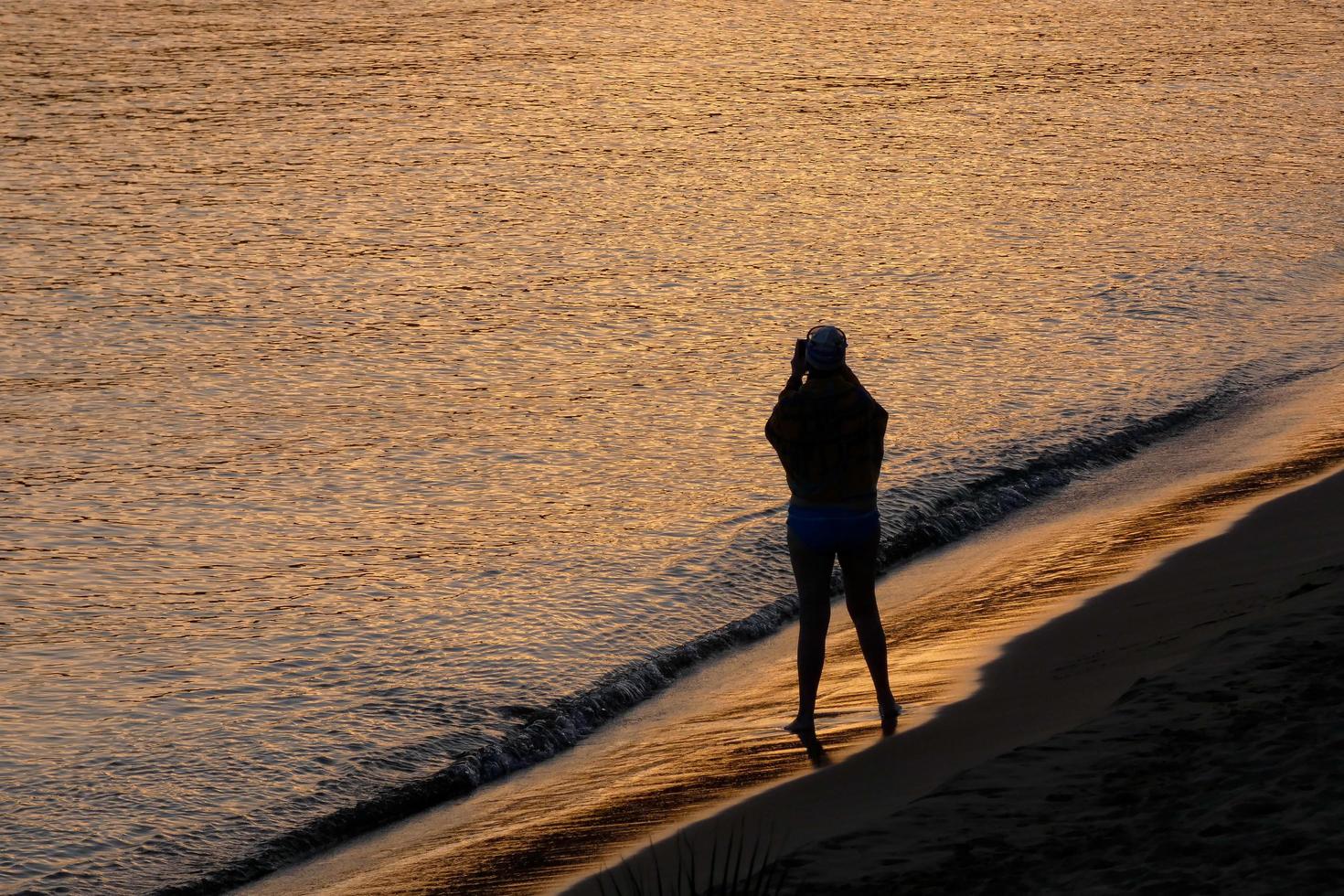 Backlight of a silhouette of an anonymous woman taking photos in the sea