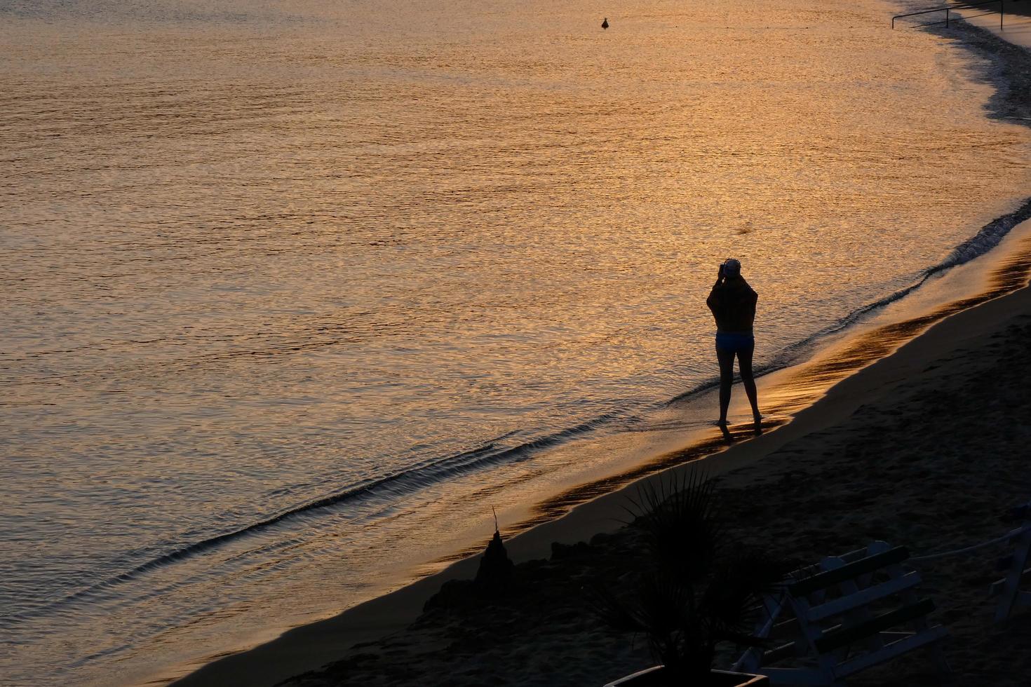 Backlight of a silhouette of an anonymous woman taking photos in the sea