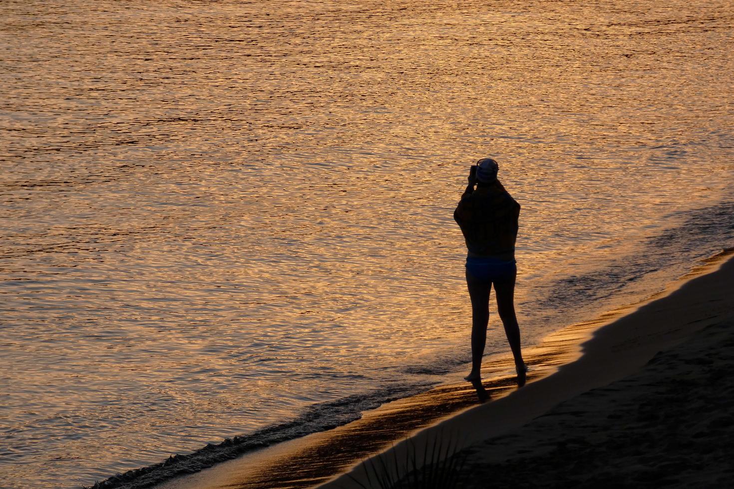 Backlight of a silhouette of an anonymous woman taking photos in the sea