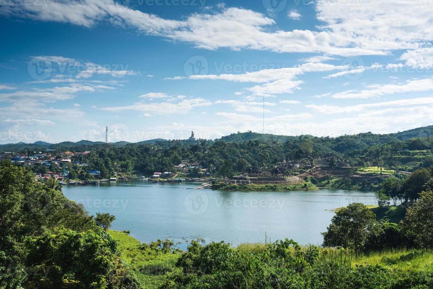 paisaje de la aldea de mon en la orilla del río y la gran estatua de buda en la colina en la selva tropical en la presa en sangkhlaburi foto