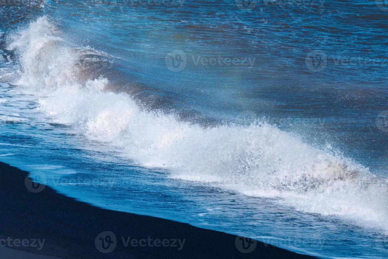 Blue ocean wave with splashing hitting on black sand beach in summer photo