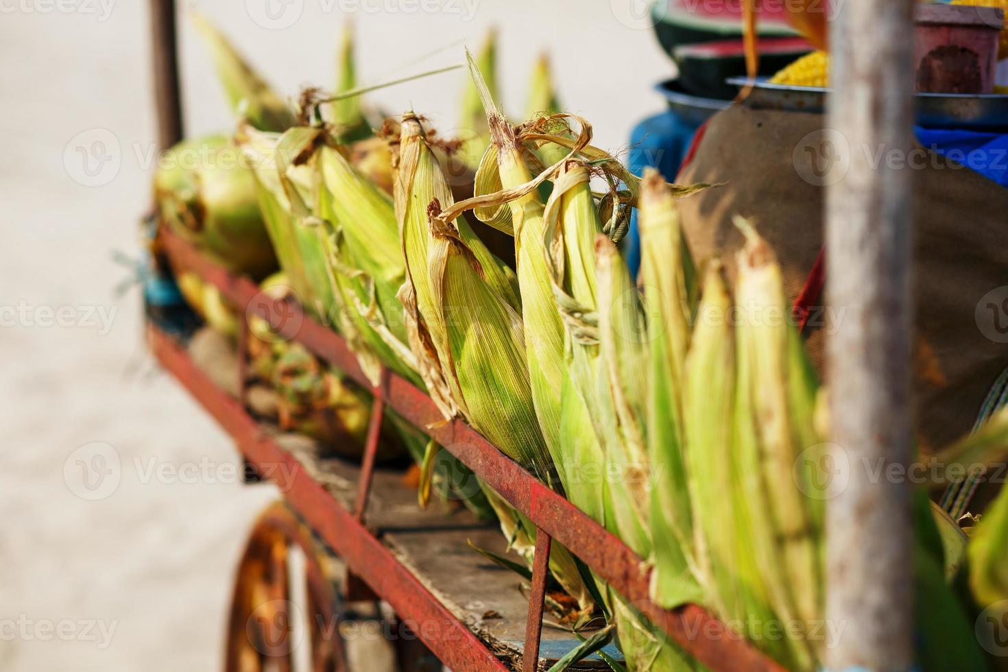 Many corn cobs in the cart. Rows of corn in the shell, lay in piles. Indian, Asian street food. Beach at GOA Sunset photo