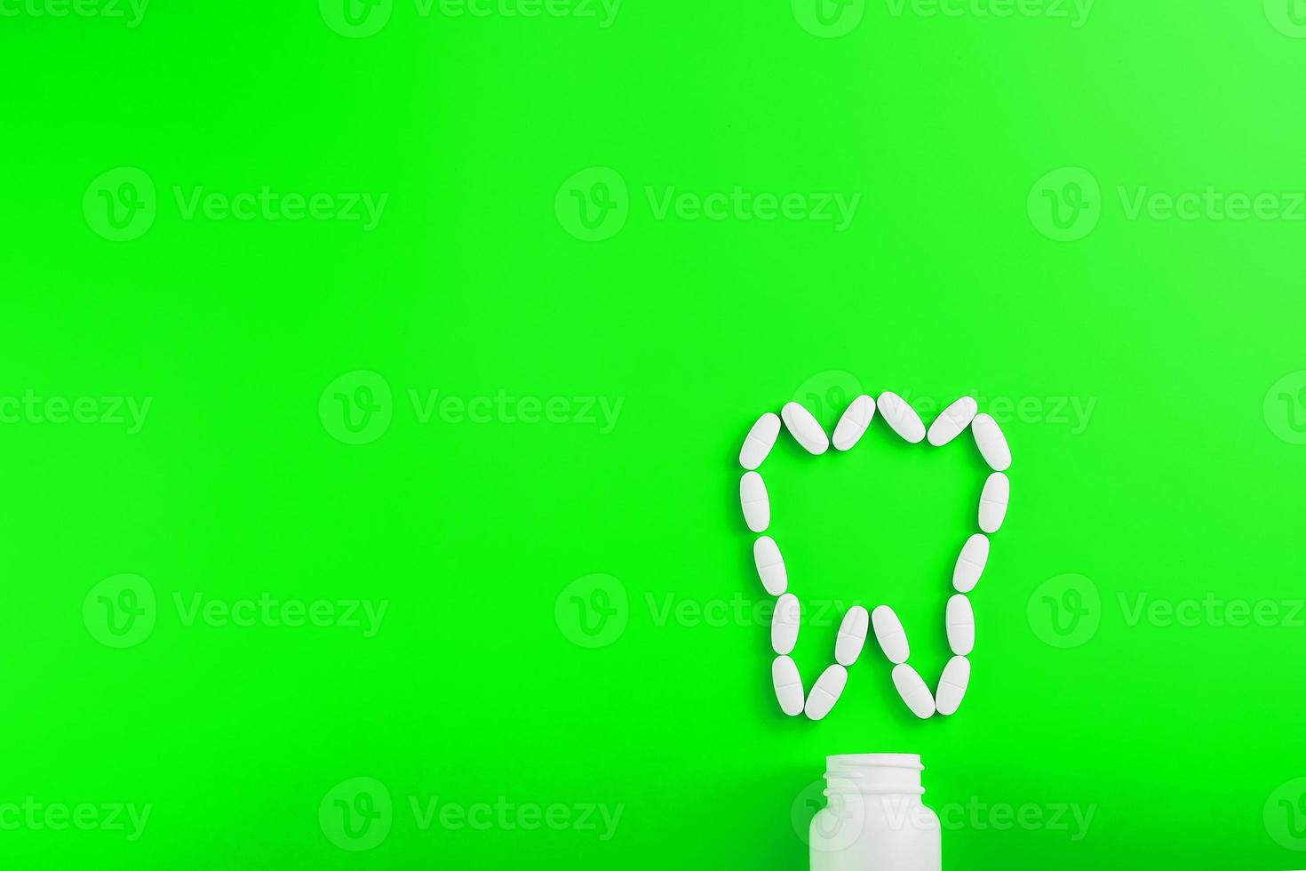 Calcium vitamin in the form of a tooth spilled out of a white jar on a Green background. photo