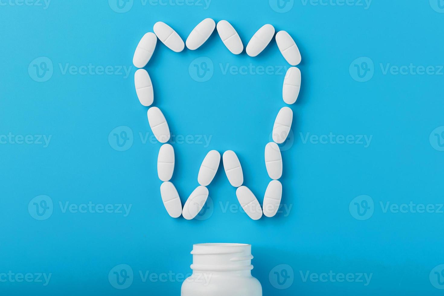 vitaminas blancas con calcio ca, d3 en forma de diente esparcido de un frasco blanco sobre un fondo azul foto