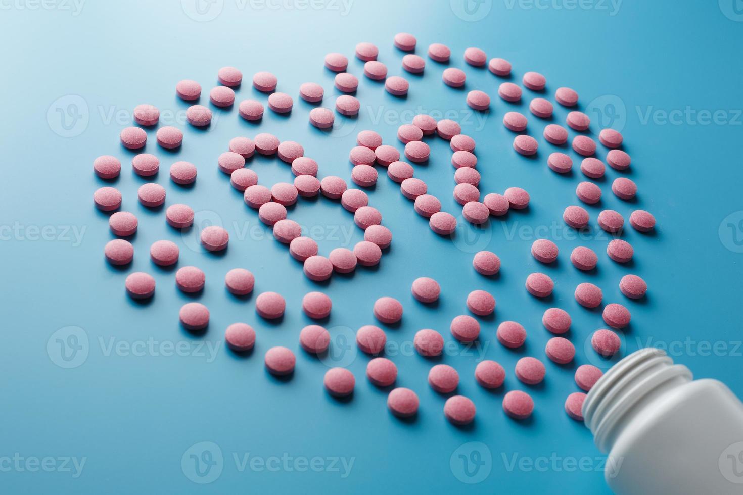 Pink tablets in the form of vitamins B12 in the heart on a blue background, spilled from a white can low contrast photo